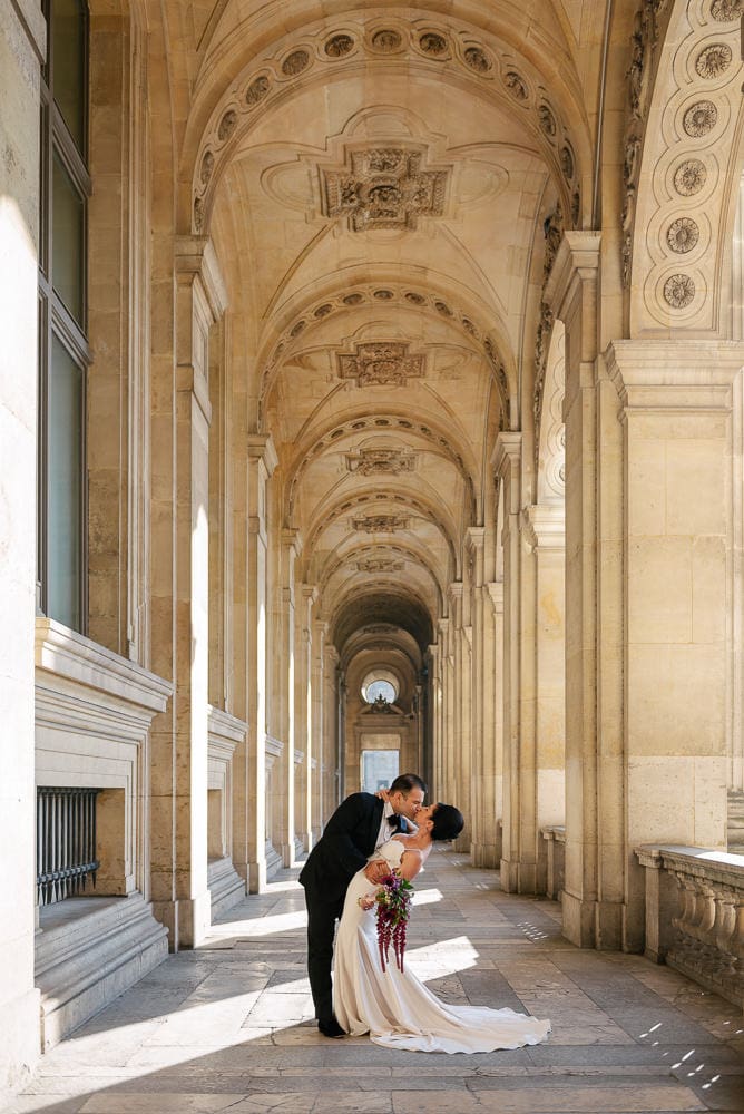 Bride and groom kissing romantically under the elegant arches of the Louvre Museum architecture Bride and groom kissing romantically under the elegant arches of the Louvre Museum architecture