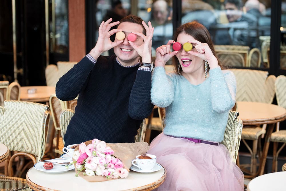 Couple having fun with colorful macarons in a parisian café Couple having fun with colorful macarons in a parisian café