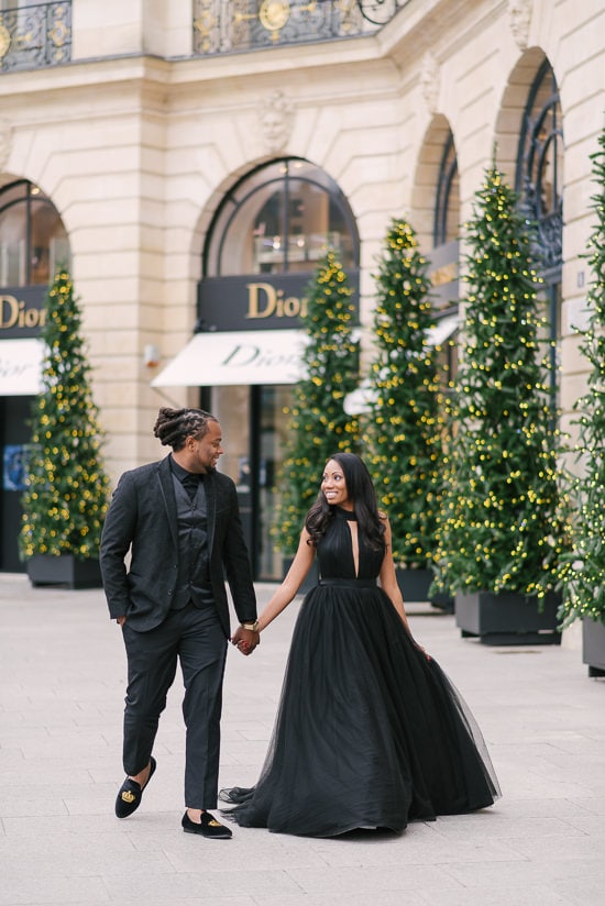 Cute couple walking holding in hands in front of Dior store in Place Vendome - beautiful Christmas decoration in the background