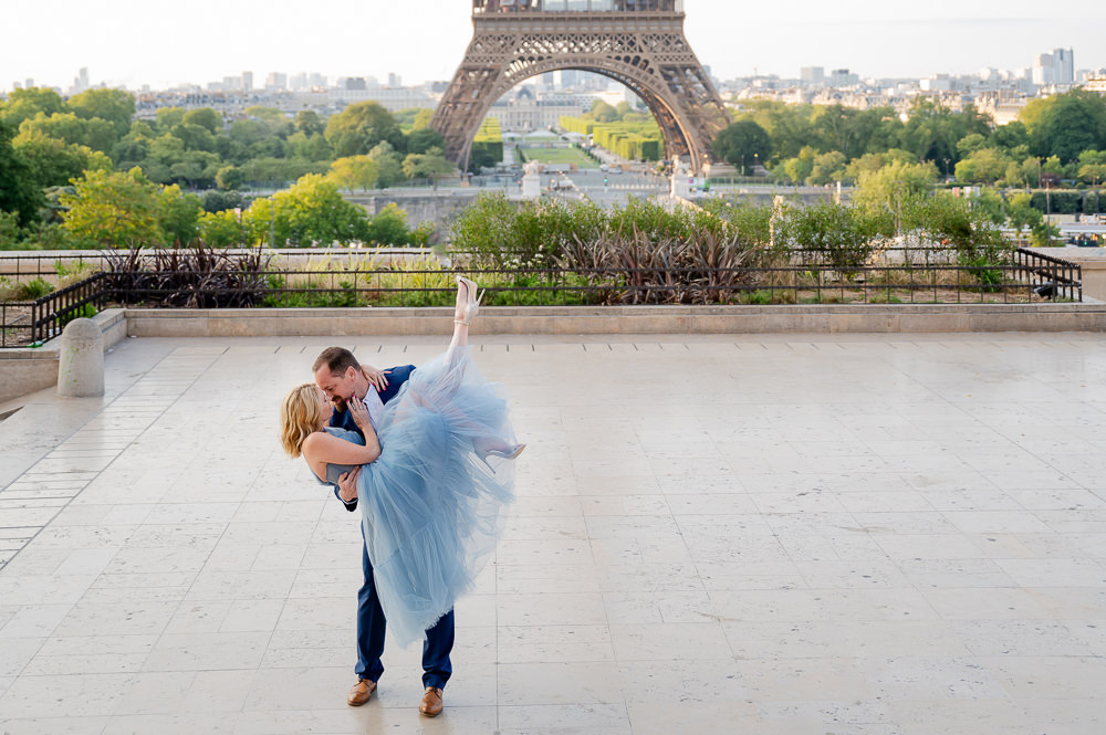 Groom dipping his partner in a blue tulle gown for a kiss at Trocadéro, the Eiffel Tower behind at sunrise